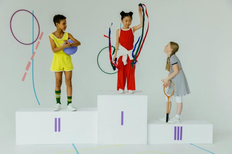 Three happy children celebrating on a gymnastics podium with equipment.