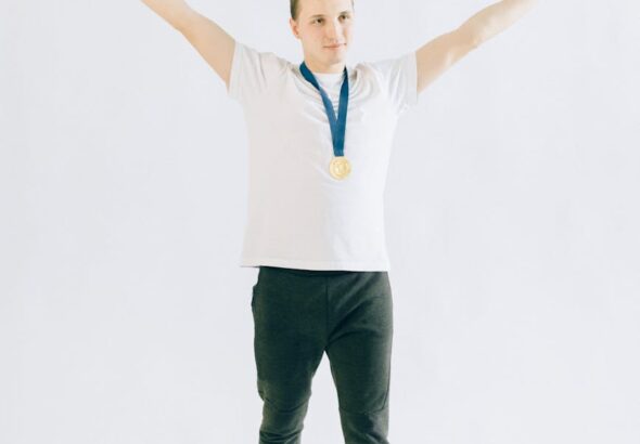 Man celebrating victory with a gold medal, arms raised, on a white background.