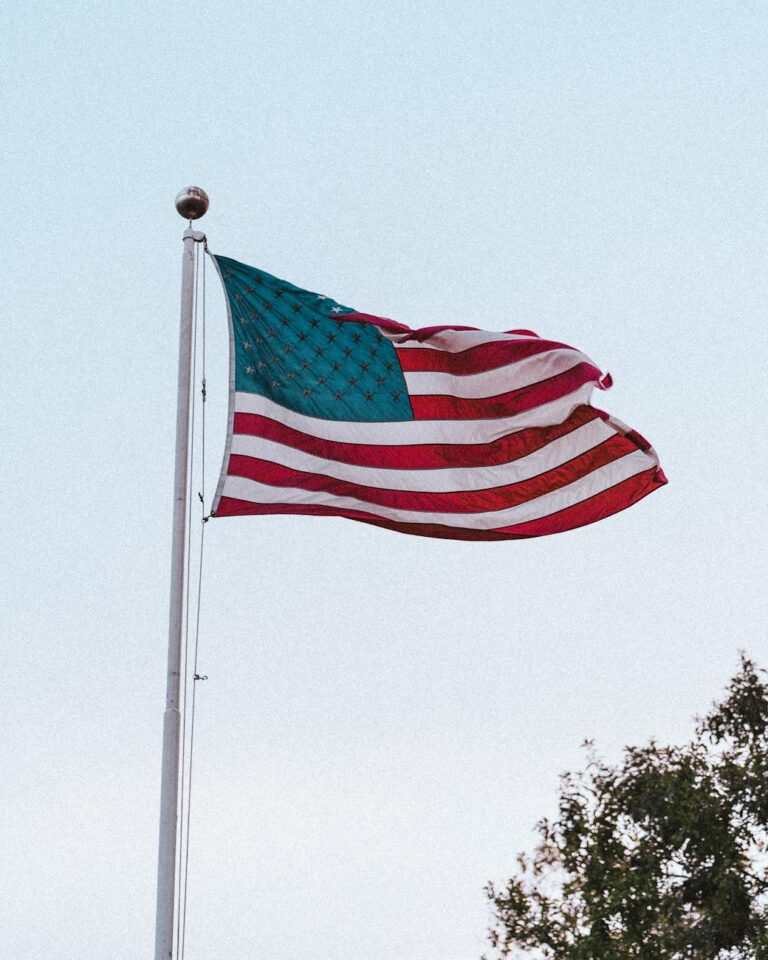 Close-up of the American flag waving on a flagpole with a clear sky backdrop.