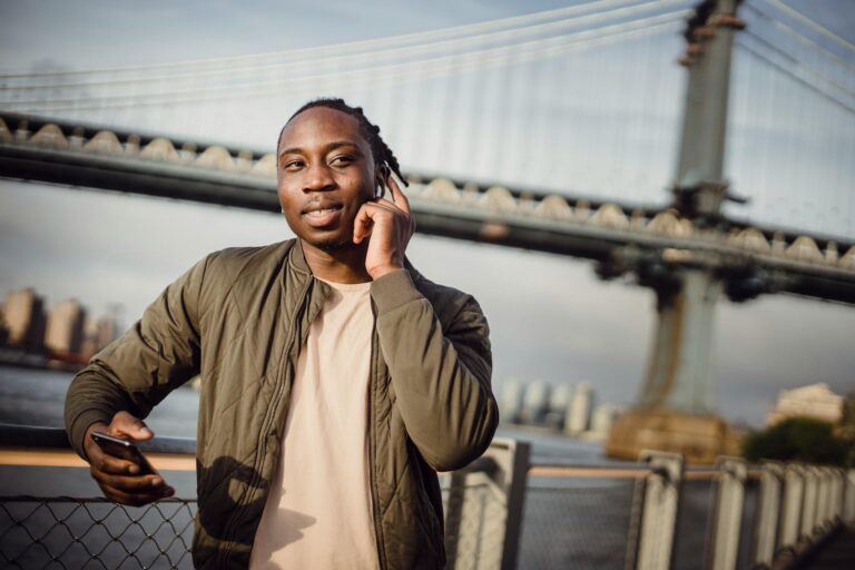 Young man talking on phone outdoors with a famous bridge in background during the day.