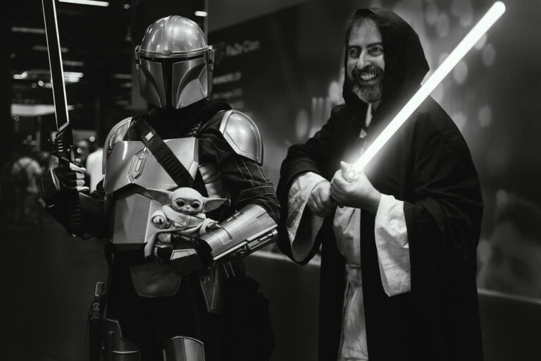 Star Wars fans in Mandalorian and Jedi costumes wielding swords at an event.