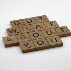 Close-up of wooden Scrabble tiles spelling 'But What About You' on a white surface.