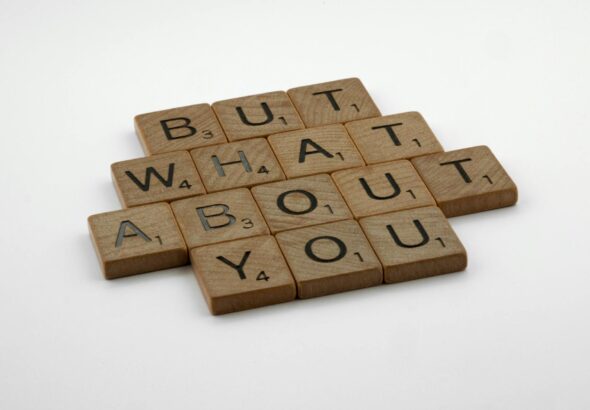 Close-up of wooden Scrabble tiles spelling 'But What About You' on a white surface.