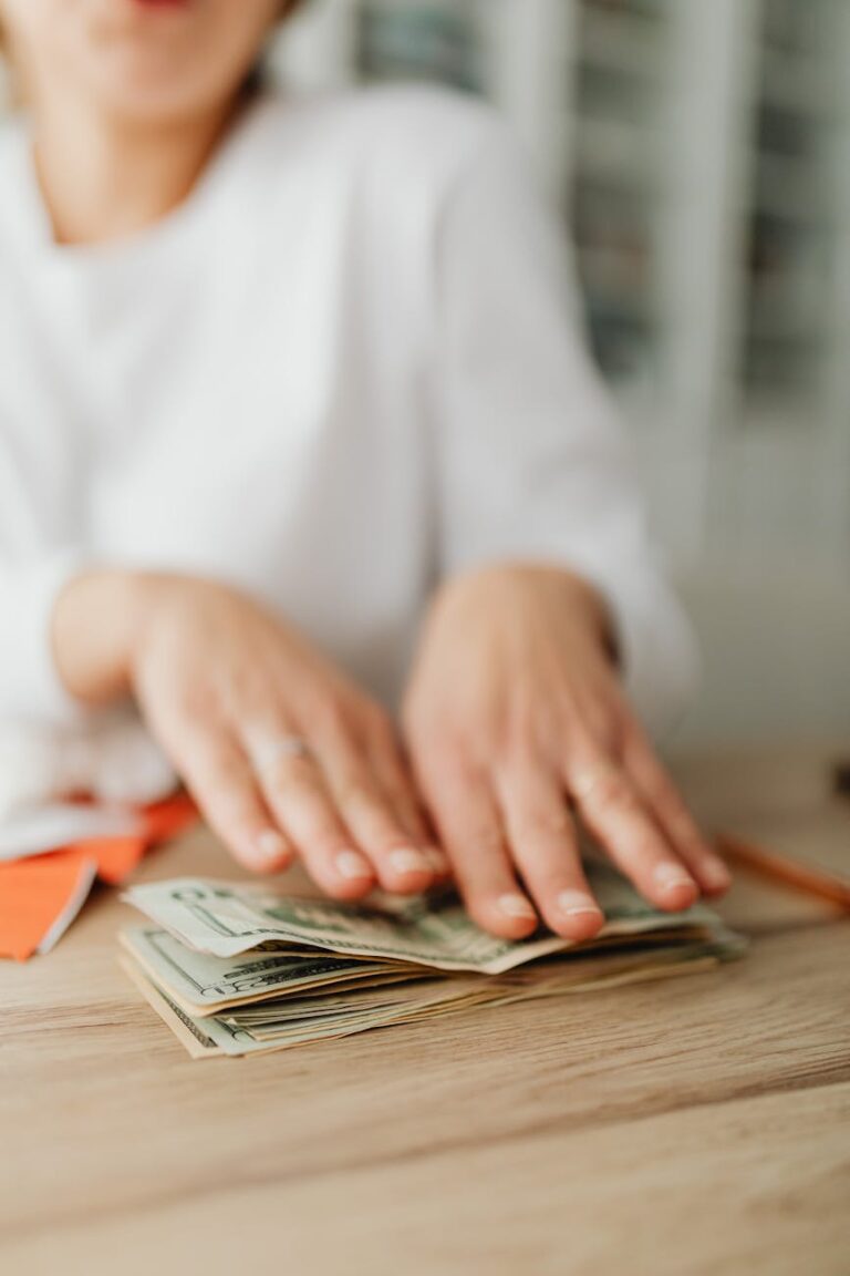 Close-up of a woman counting cash at a wooden desk, focusing on hands and banknotes.