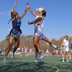 Dynamic capture of a netball match on a sunny day, featuring female athletes in action.