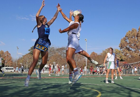 Dynamic capture of a netball match on a sunny day, featuring female athletes in action.