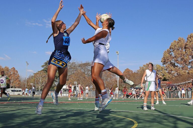 Dynamic capture of a netball match on a sunny day, featuring female athletes in action.