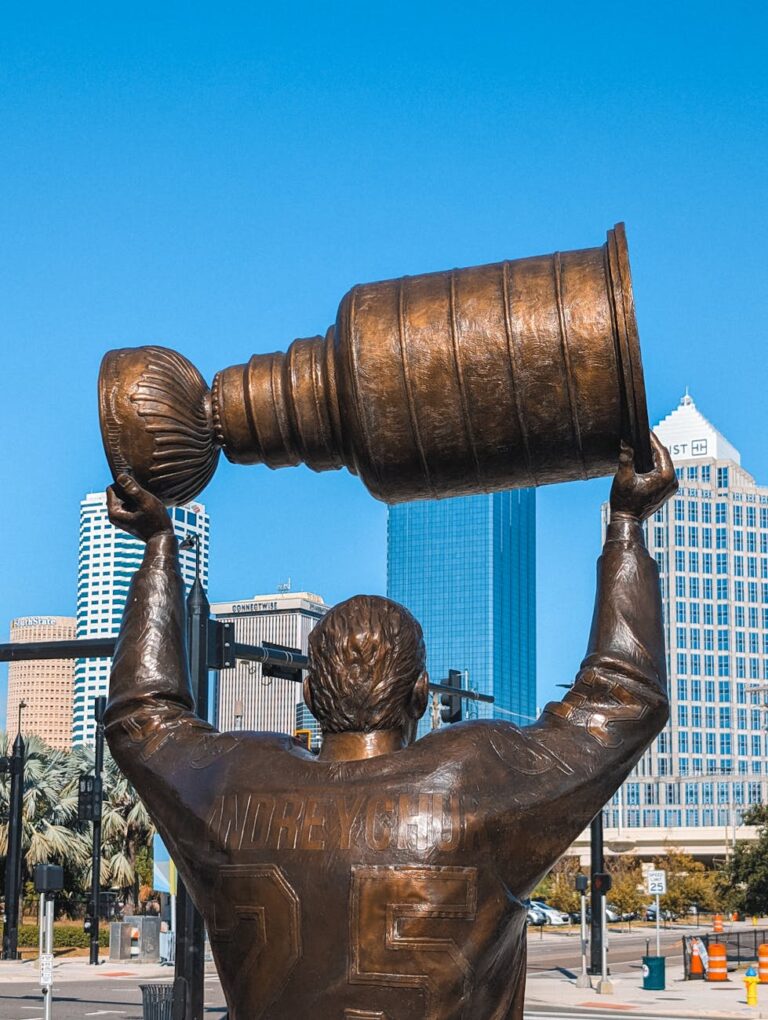 Bronze statue of a hockey player lifting the Stanley Cup in Tampa's urban landscape.