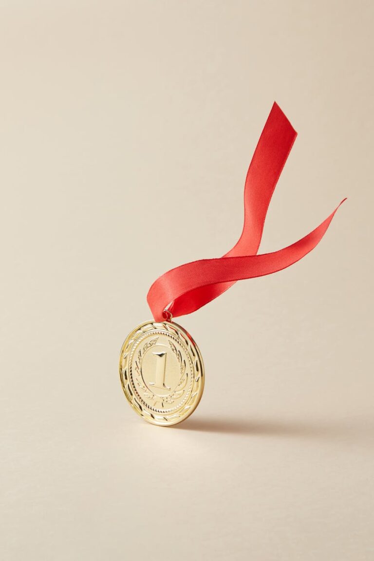 Close-up of a gold medal with red ribbon on a beige background, representing victory and achievement.