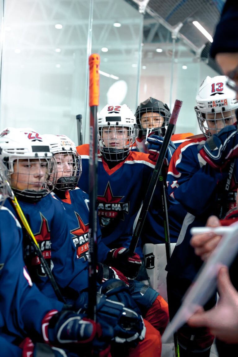 Young ice hockey players huddle with coach for strategy in indoor arena.