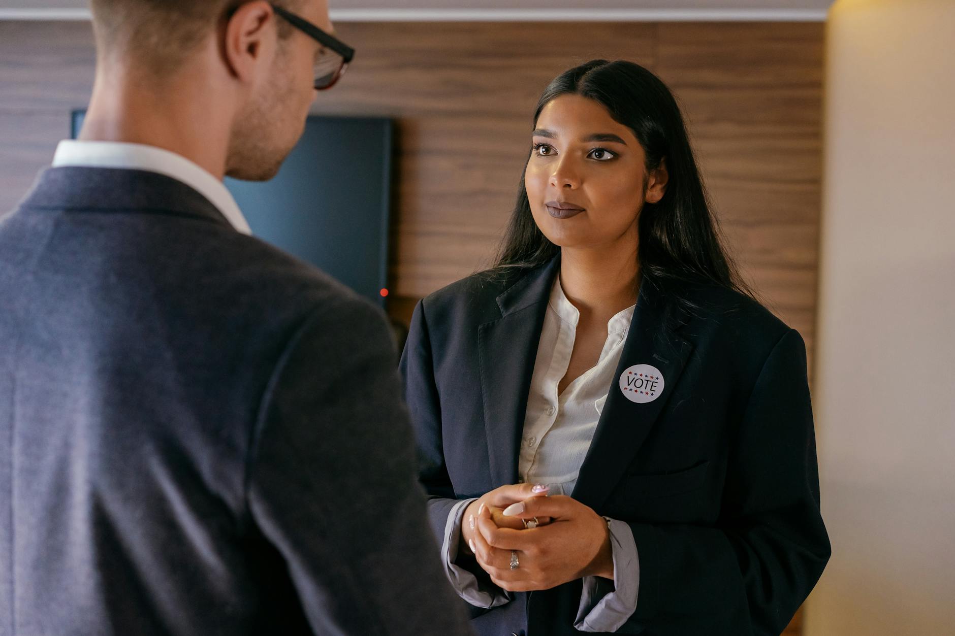 A female candidate in a political discussion, wearing a vote badge during an election campaign indoors.